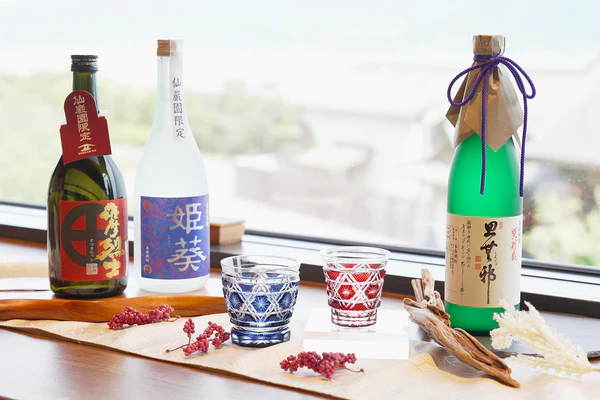 島津薩摩切子のグラスと芋焼酎ボトルが窓辺に並び、手前には秋の装飾が添えられている。