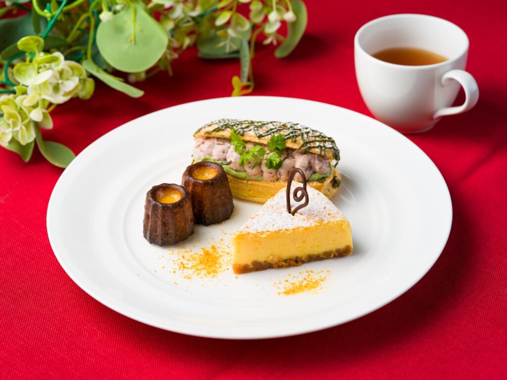 白いプレートに小さな焼き菓子やケーキなどが盛りつけられ、紅茶カップと緑の装飾が添えられている