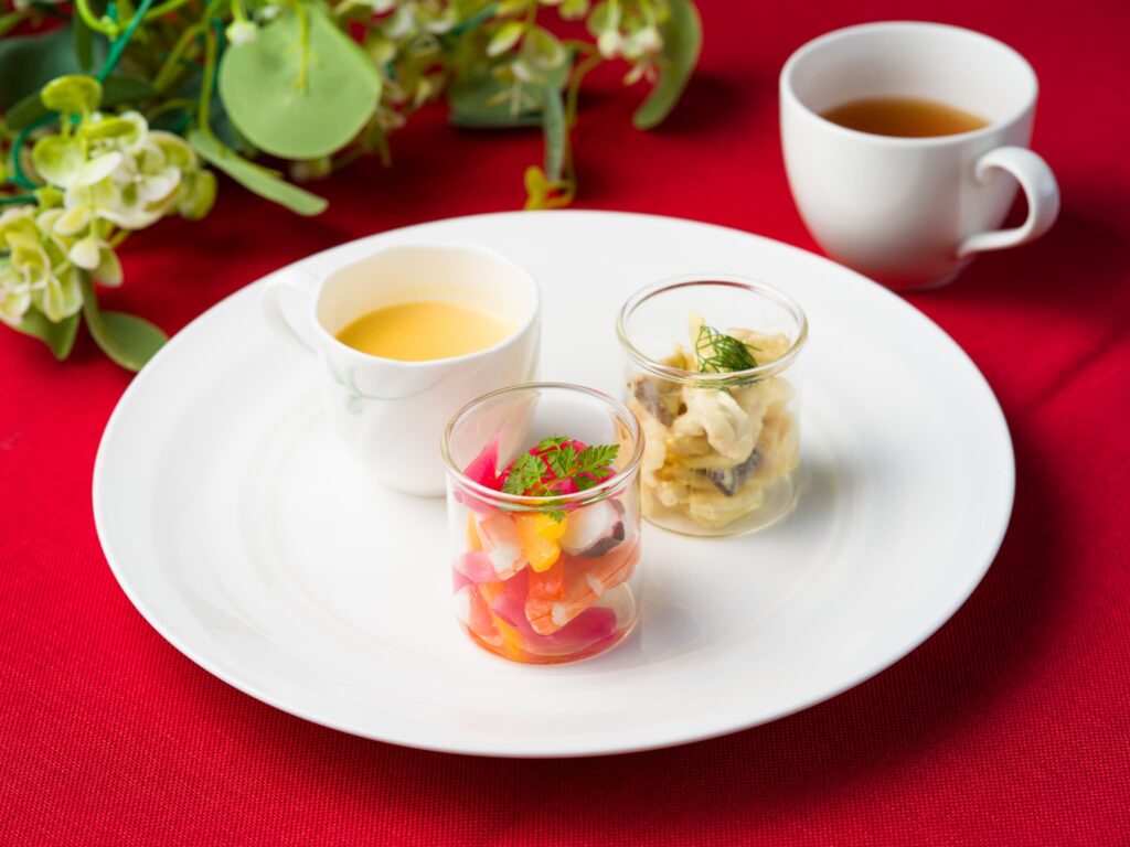 白いプレートにスープなどが並び、紅茶カップと緑の装飾が添えられている