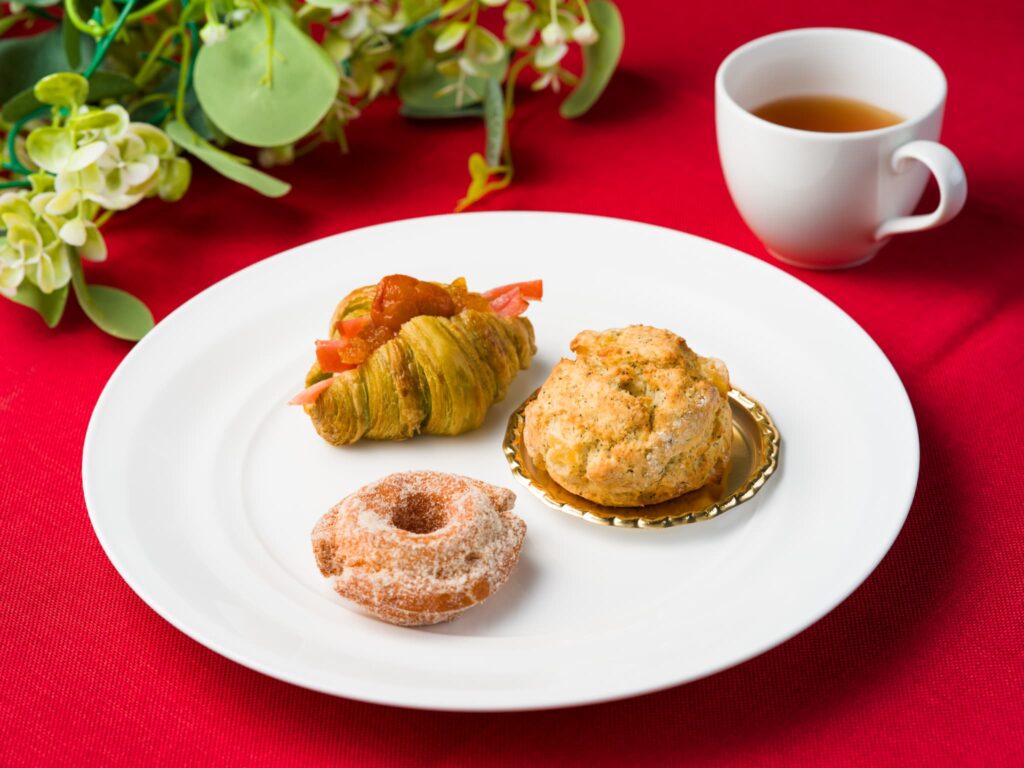 白いプレートにスコーンや焼き菓子などが盛りつけられ、紅茶カップと緑の装飾が添えられている